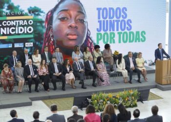 Várias pessoas sentadas num palco ouvem um homem discursar
